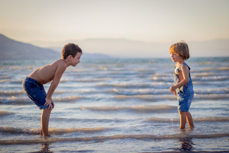 Family Beaches - boy bending knee while watching younger child on beach