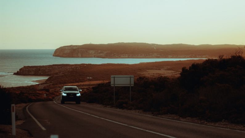 Farm Stays - a car driving down a road next to a body of water